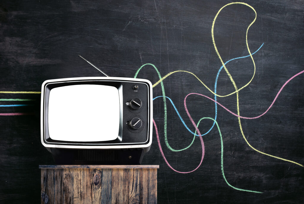 Vintage tv in front of a blackboard. There are multicoloured lines drawn on the chalkboard. The lines are straight up to the tv coming out distorted. Propaganda or disinformation concept