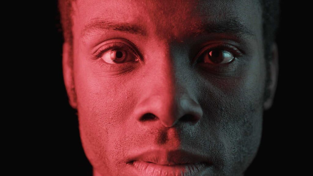 Close-up portrait of Desmond Cole, harshly lit from one side by red light.